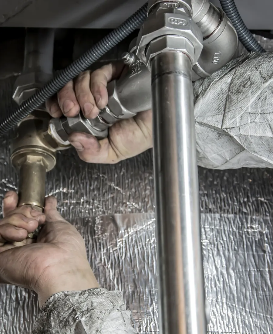 Plumber connecting steel pipework under a sink