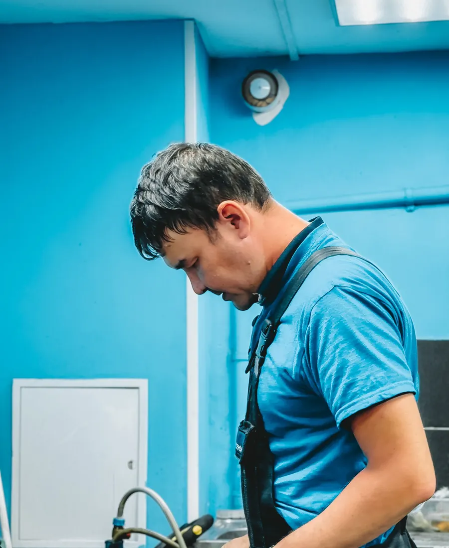 Plumber in a blue uniform working at a bench in a blue workshop