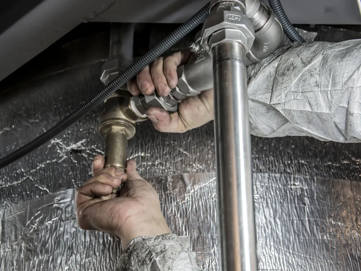 Plumber connecting steel pipework under a sink